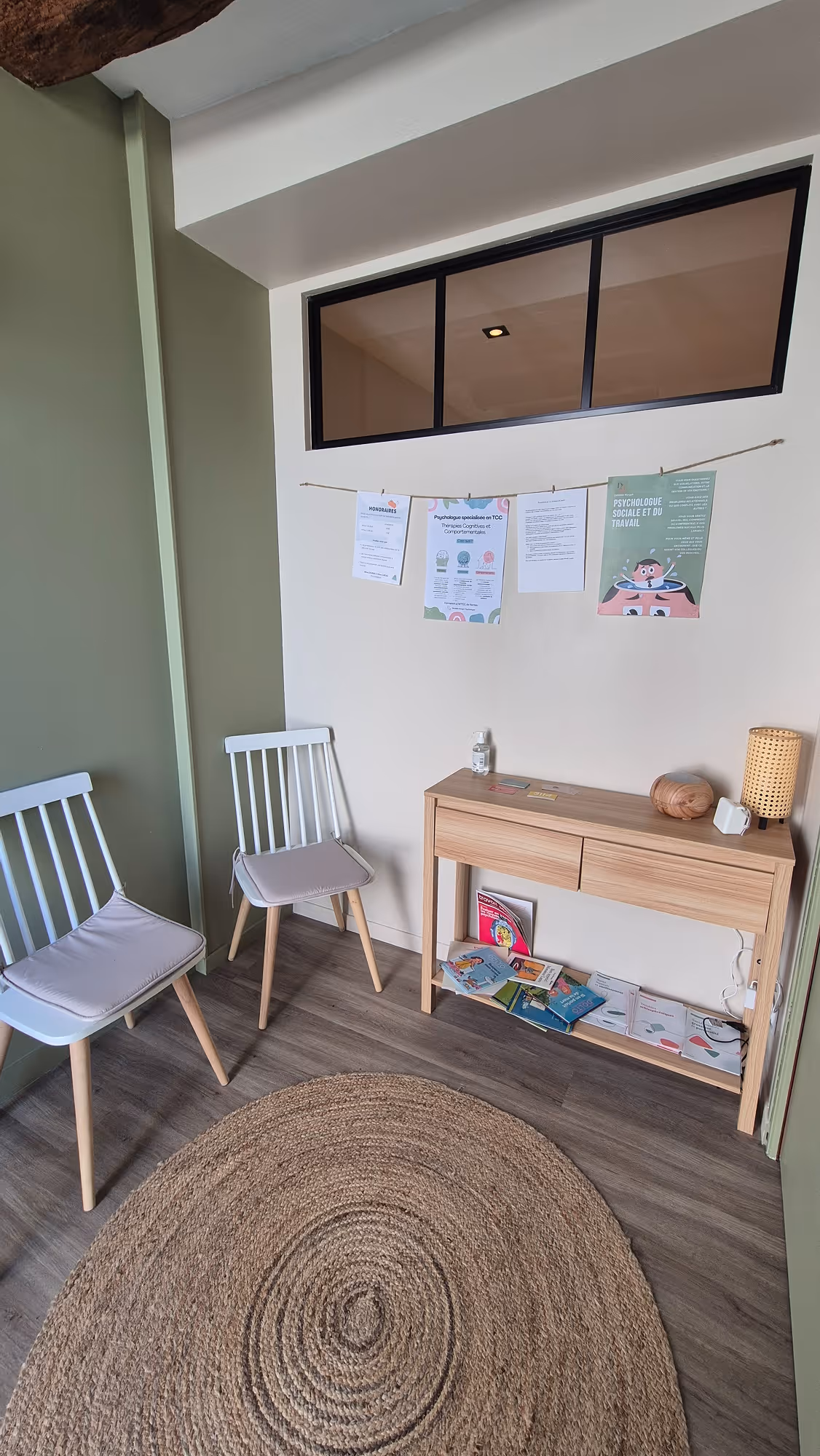 Salle d'attente du cabinet de Margot Daubas, psychologue libérale TCC à la Possonnière, près d'Angers. Salle d'attente équipée de deux chaises blanches, d'une console en bois, d'un tapis rond tissé et d'affiches d'information accrochées au mur.