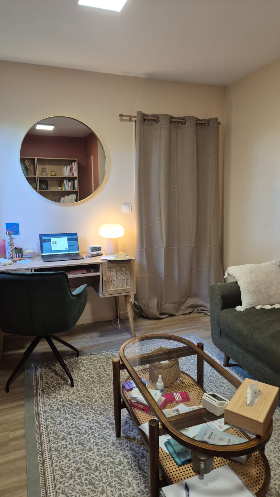 Cabinet de Margot Daubas, psychologue TCC à la Possonnière, près d'Angers. Une pièce chaleureuse et confortable avec un bureau, un ordinateur portable, une lampe, une chaise, une table basse en verre et un canapé vert orné d'un coussin.