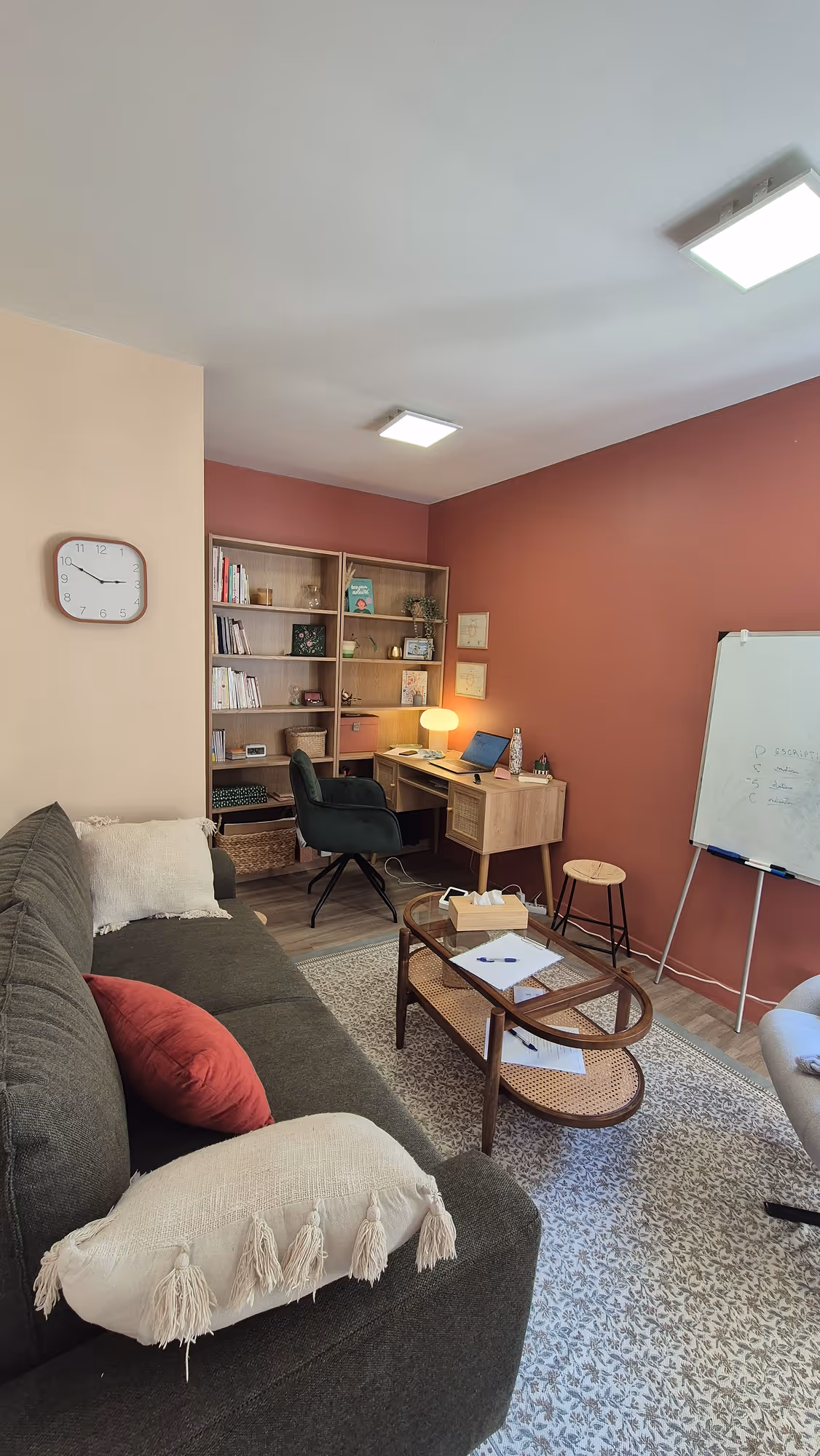 Cabinet de Margot Daubas, psychologue TCC à la Possonnière, près d'Angers. Un bureau chaleureux avec un canapé, des coussins colorés, une table basse en verre, un bureau en bois et un tableau blanc accroché au mur.