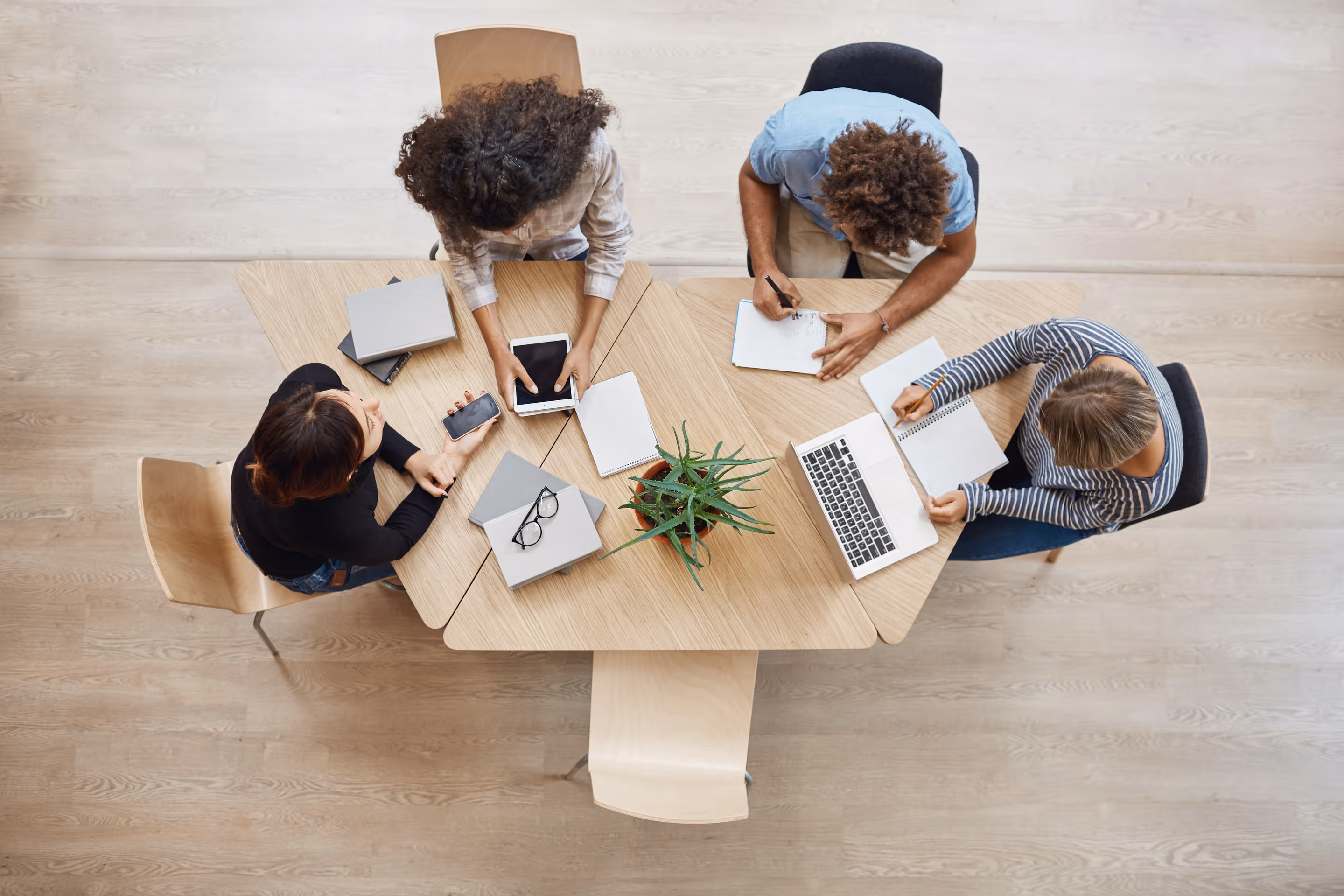 Vue aérienne de quatre personnes assises à une table, en train de travailler, entourées d'ordinateurs portables et de carnets de notes.